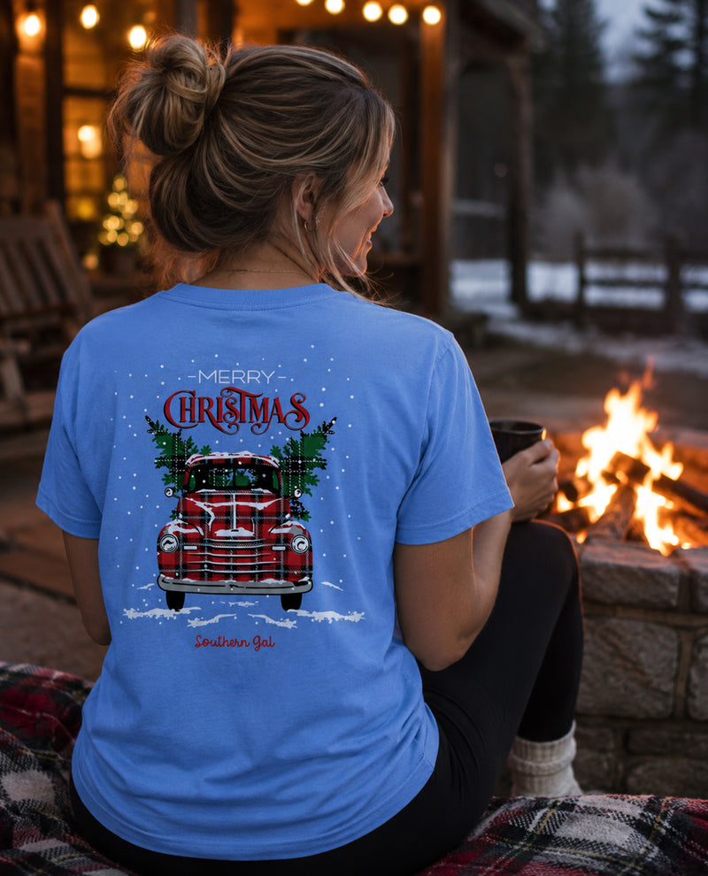 Woman wearing a blue t-shirt with a Christmas design, sitting by a fire.
