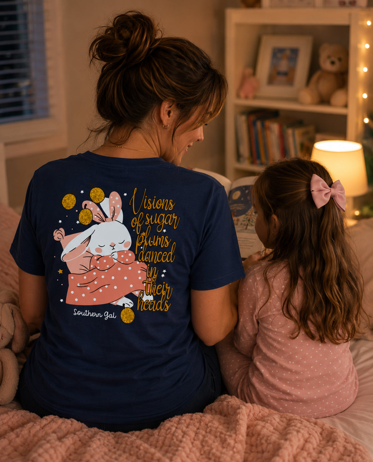 Woman wearing a navy blue t-shirt with a graphic and text, sitting on a bed with a child.