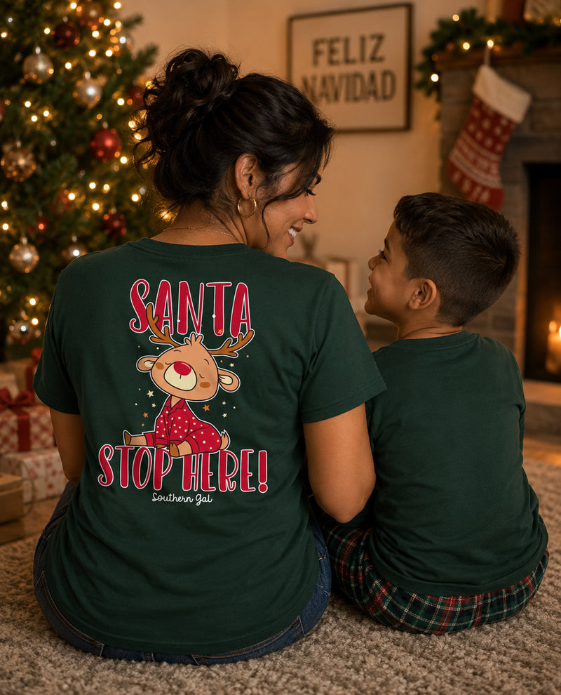 Two people wearing green t-shirts with a Christmas design in a festive room.