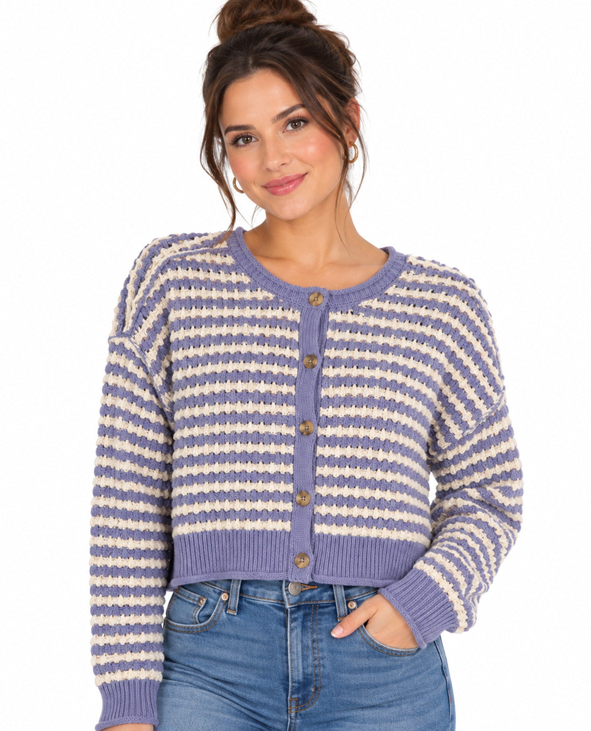 A woman wearing a lavender and cream striped knit cardigan with brown buttons, paired with blue jeans, against a plain white background.