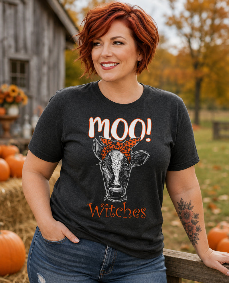 Woman wearing a black t-shirt with a cow graphic and text, standing in an autumn setting with pumpkins and a barn.