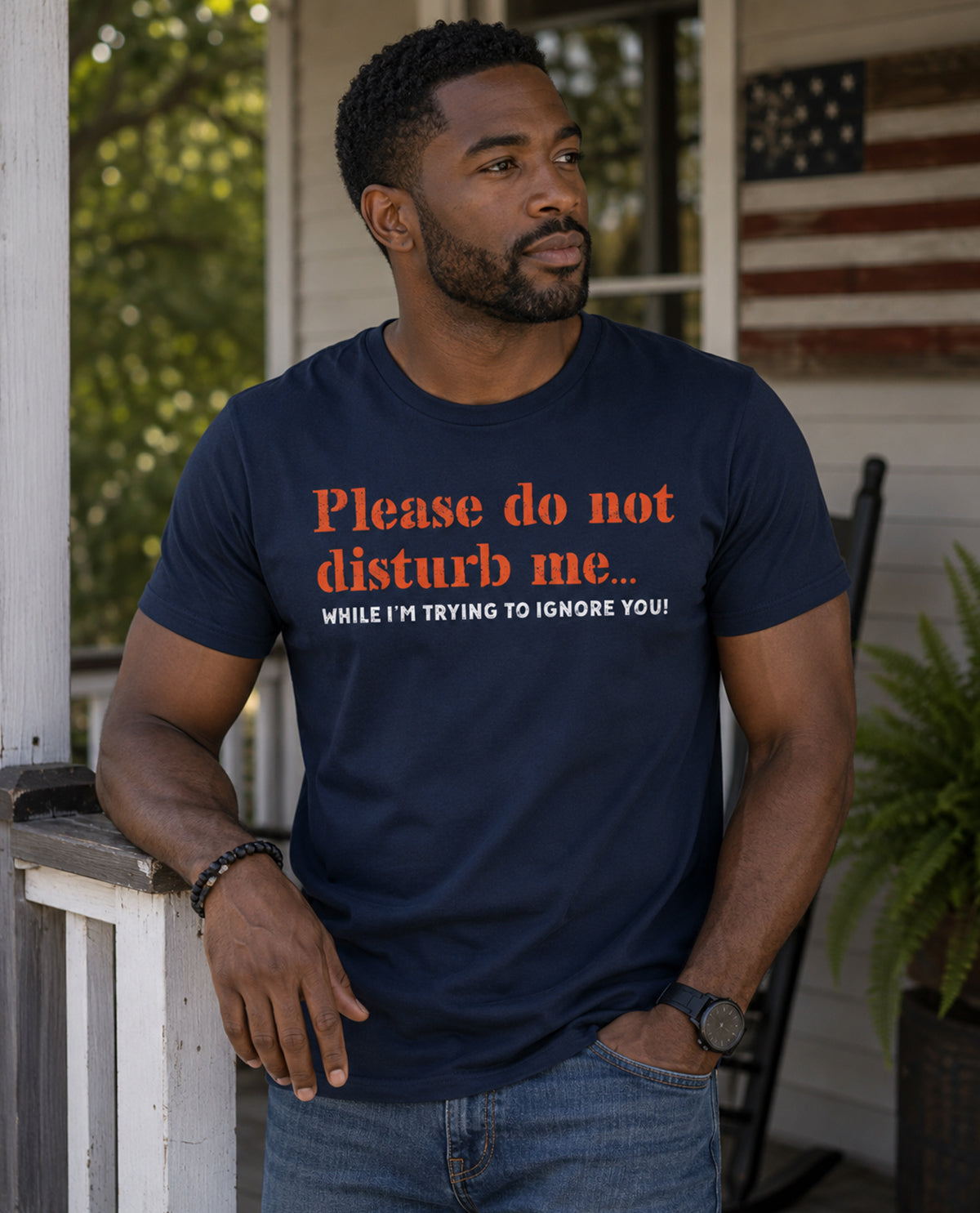 Man wearing a navy blue t-shirt with humorous text on a porch.