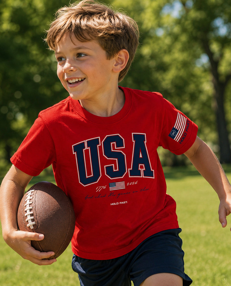 Child wearing a red 'USA' t-shirt holding a football outdoors