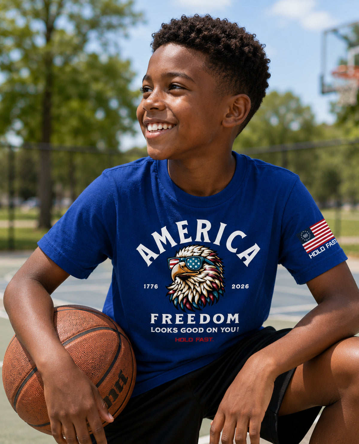 Child holding a basketball on a court wearing a blue t-shirt with 'America Freedom' design.