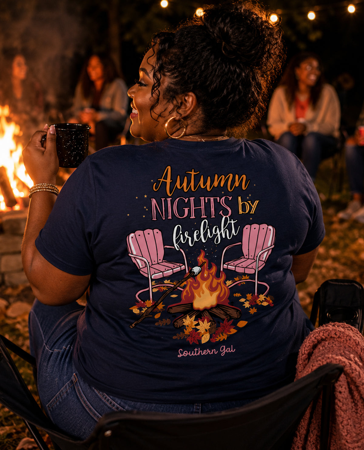 Person wearing a t-shirt with 'Autumn Nights by Firelight Southern Gal' design, sitting by a campfire.