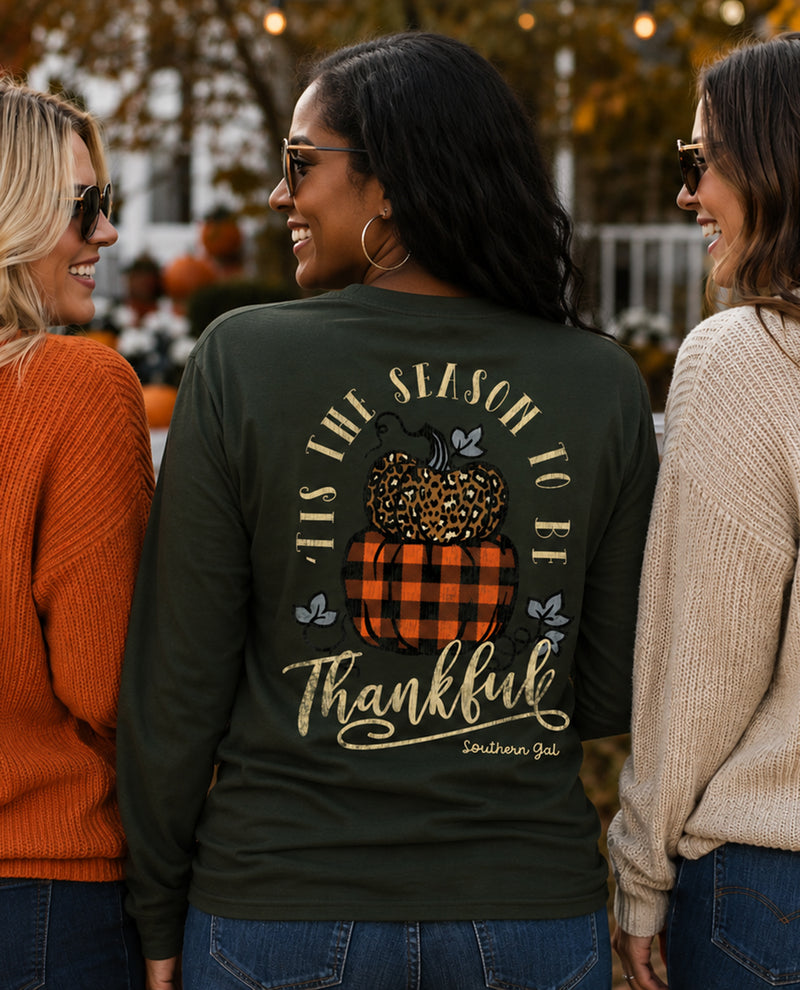 Woman wearing a green long-sleeve shirt with a pumpkin design and text, standing outdoors with two other people.