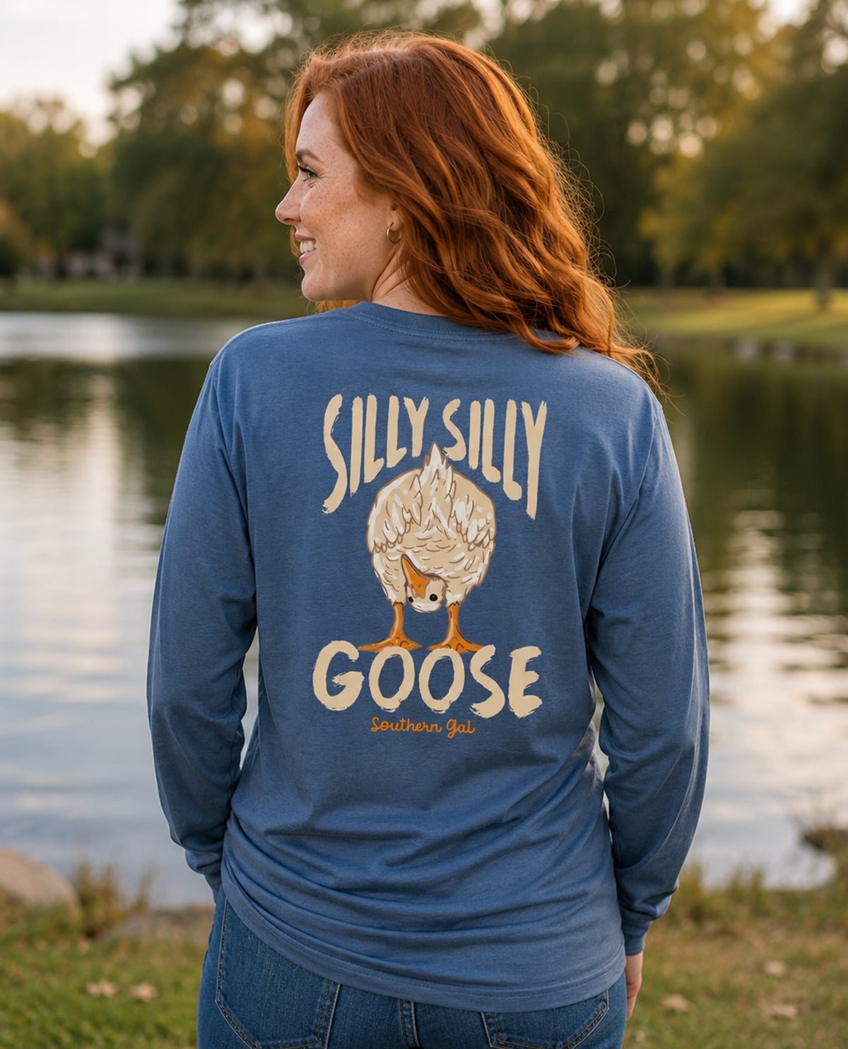 Woman wearing a blue shirt with 'Silly Silly Goose' design by a lake