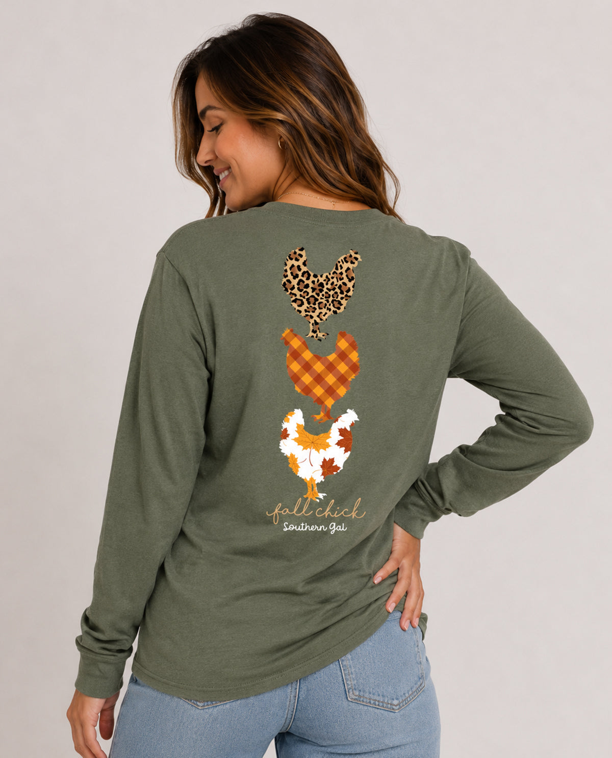 A woman wearing an olive green long-sleeve t-shirt, shown from the back. The shirt features a graphic of three stacked chickens in autumn-themed patterns (leopard print, orange plaid, white with orange accents) and the words 'fall chick southern girl' in a script font.