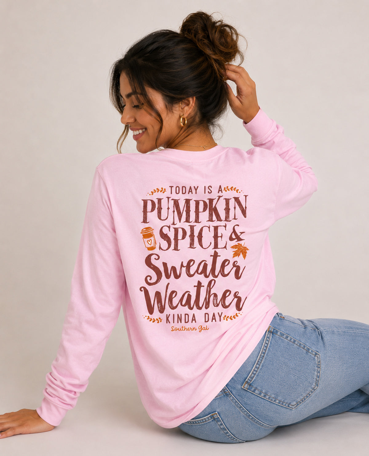 Woman wearing a pink long-sleeve shirt with 'Pumpkin Spice & Sweater Weather' text on the back.
