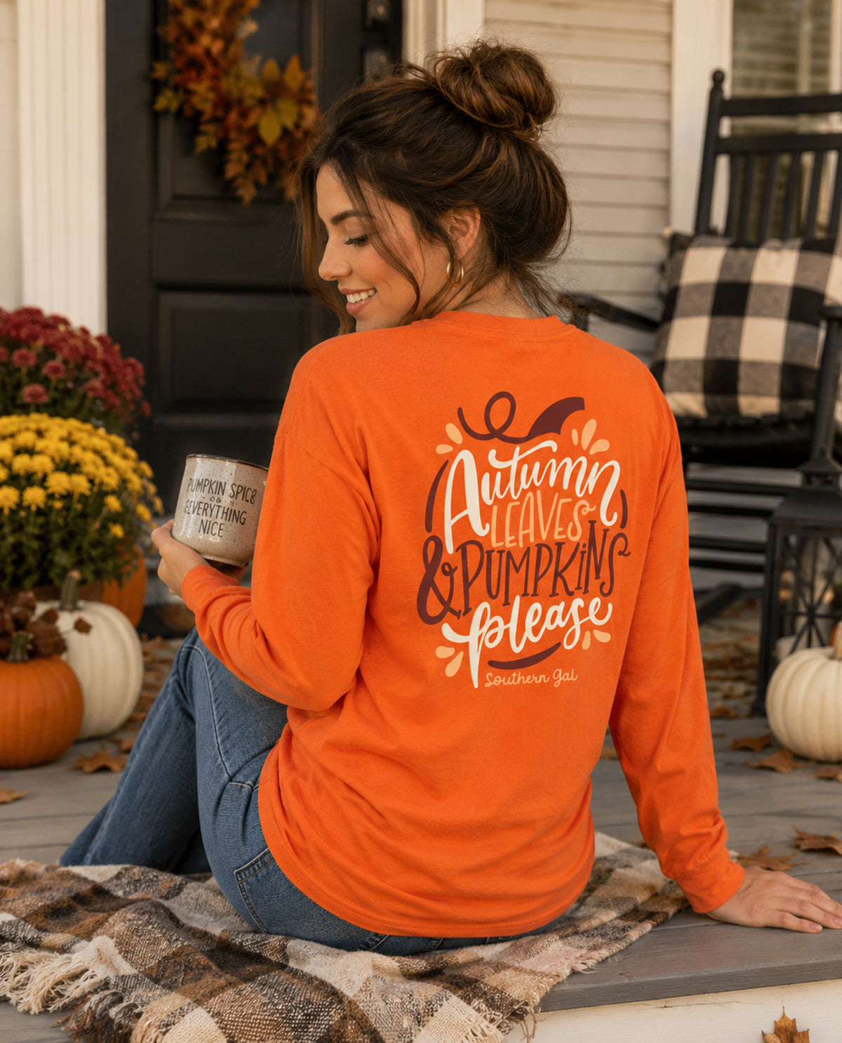 Woman wearing an orange shirt with 'Autumn Leaves & Pumpkin Please' text, sitting on a porch.