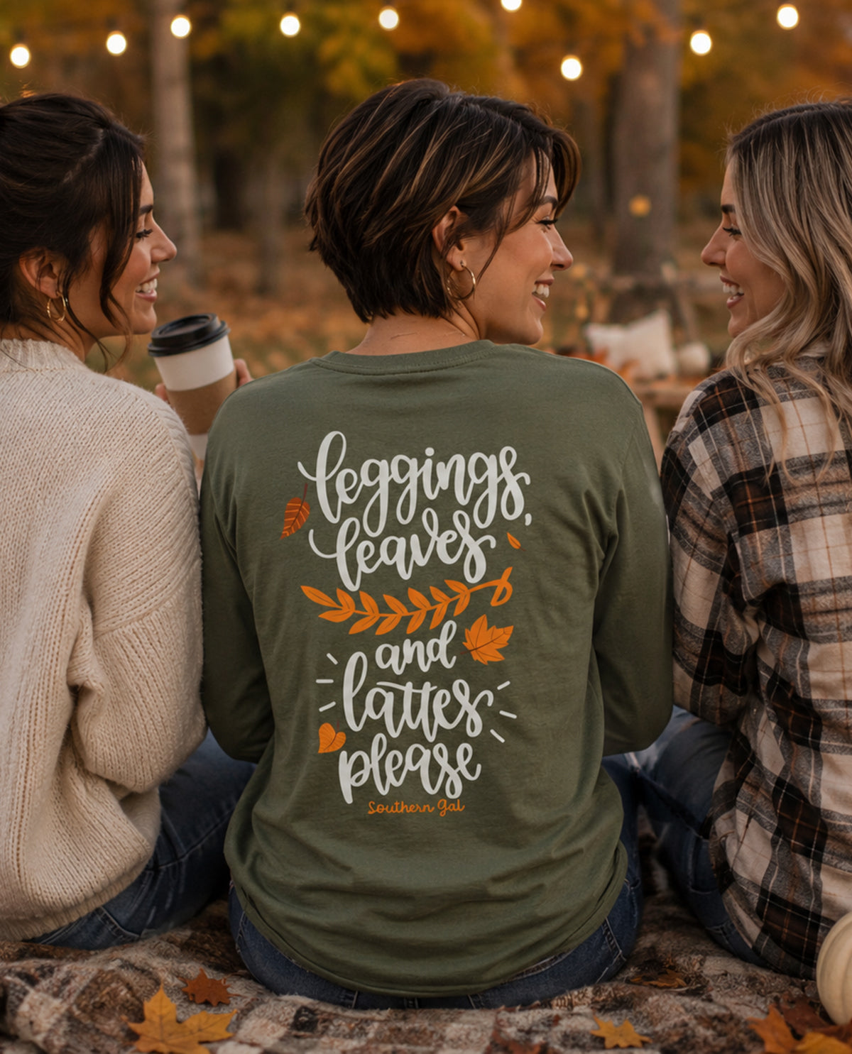 Three women sitting together with one wearing a green shirt with text and leaf graphics.