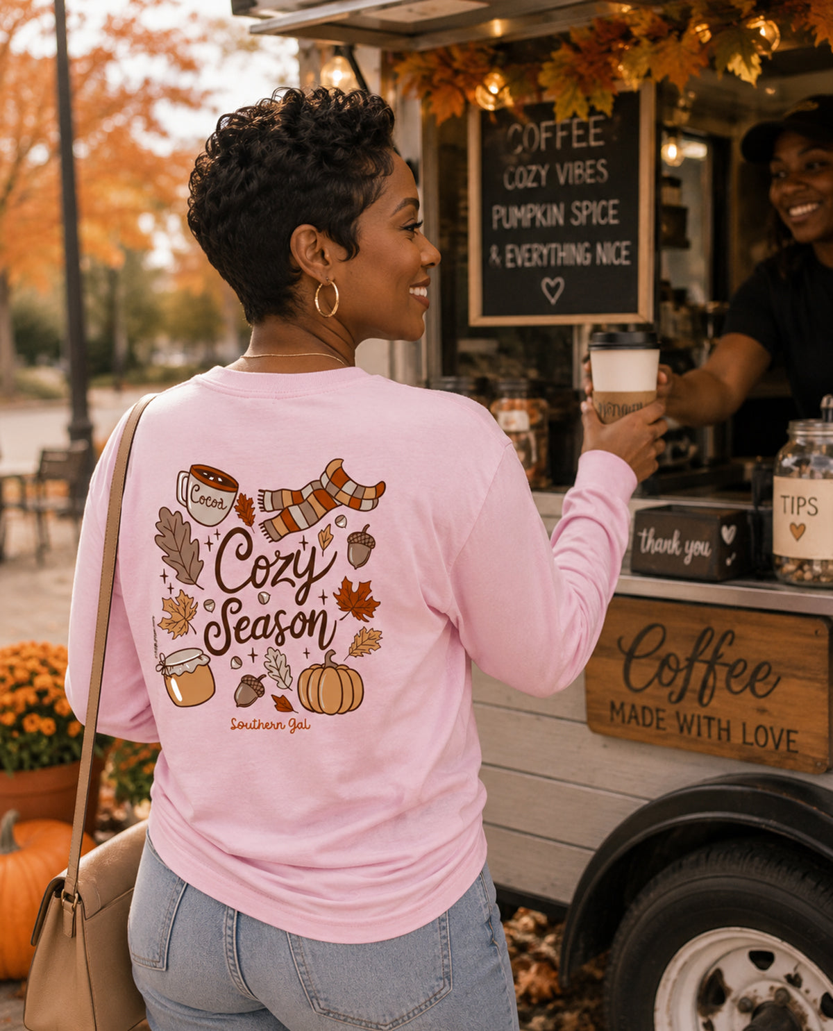 Woman wearing a pink shirt with 'Cozy Season' design, standing in front of a coffee truck.