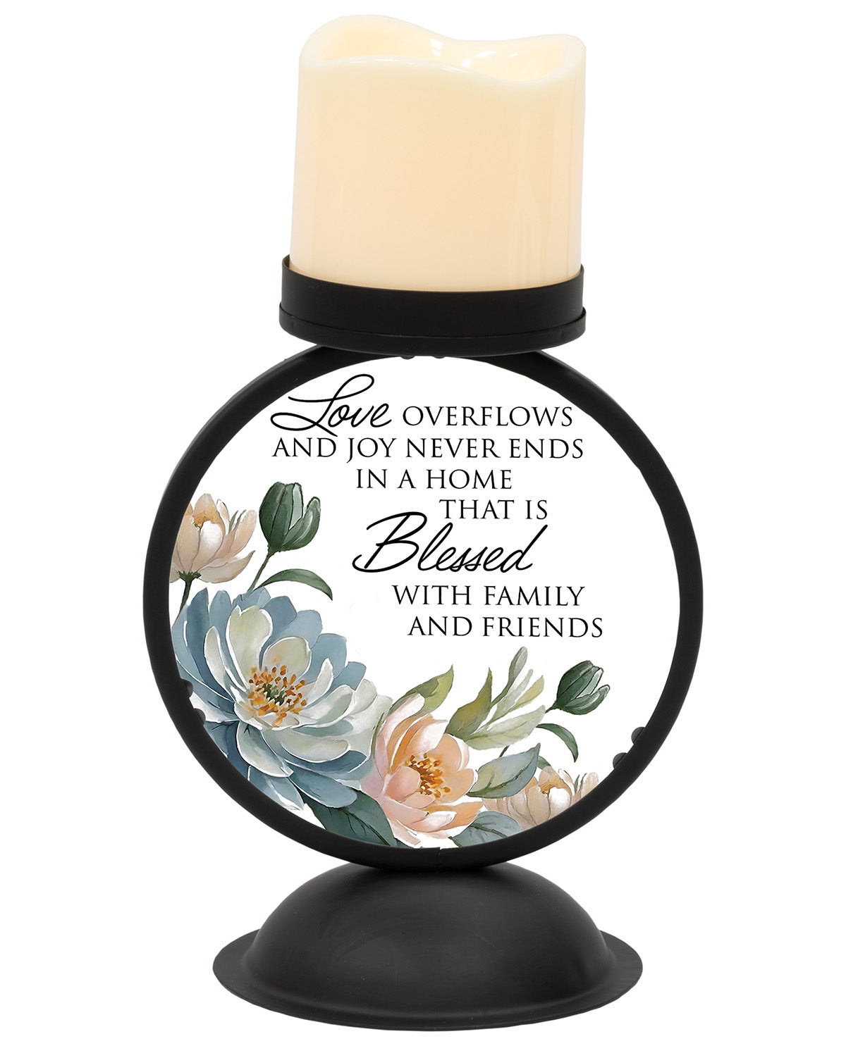 A round black metal candle holder with a black base and a cream-colored wax candle on top. The front features a white label with black text reading 'Love OVERFLOWS and JOY NEVER ENDS in a HOME that IS Blessed WITH family AND friends' surrounded by blue, white, and peach flowers.