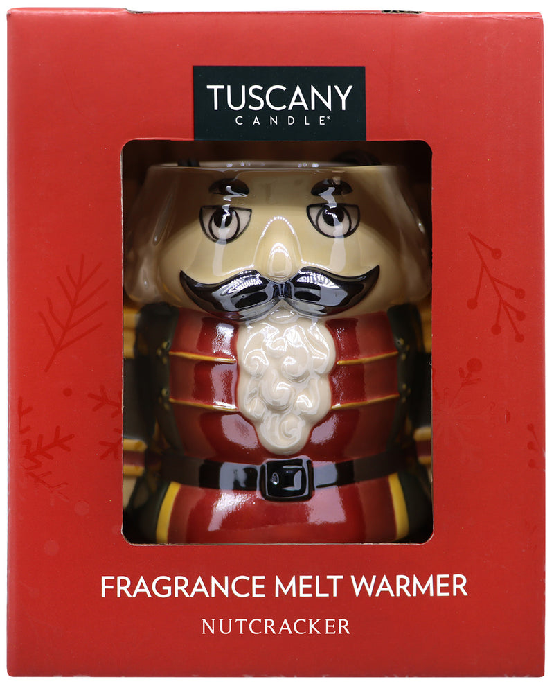 Tuscany Candle fragrance melt warmer shaped like a nutcracker, shown in its red retail box with a clear window. The product features a beige face and mustache, a red and gold uniform, and a white beard.
