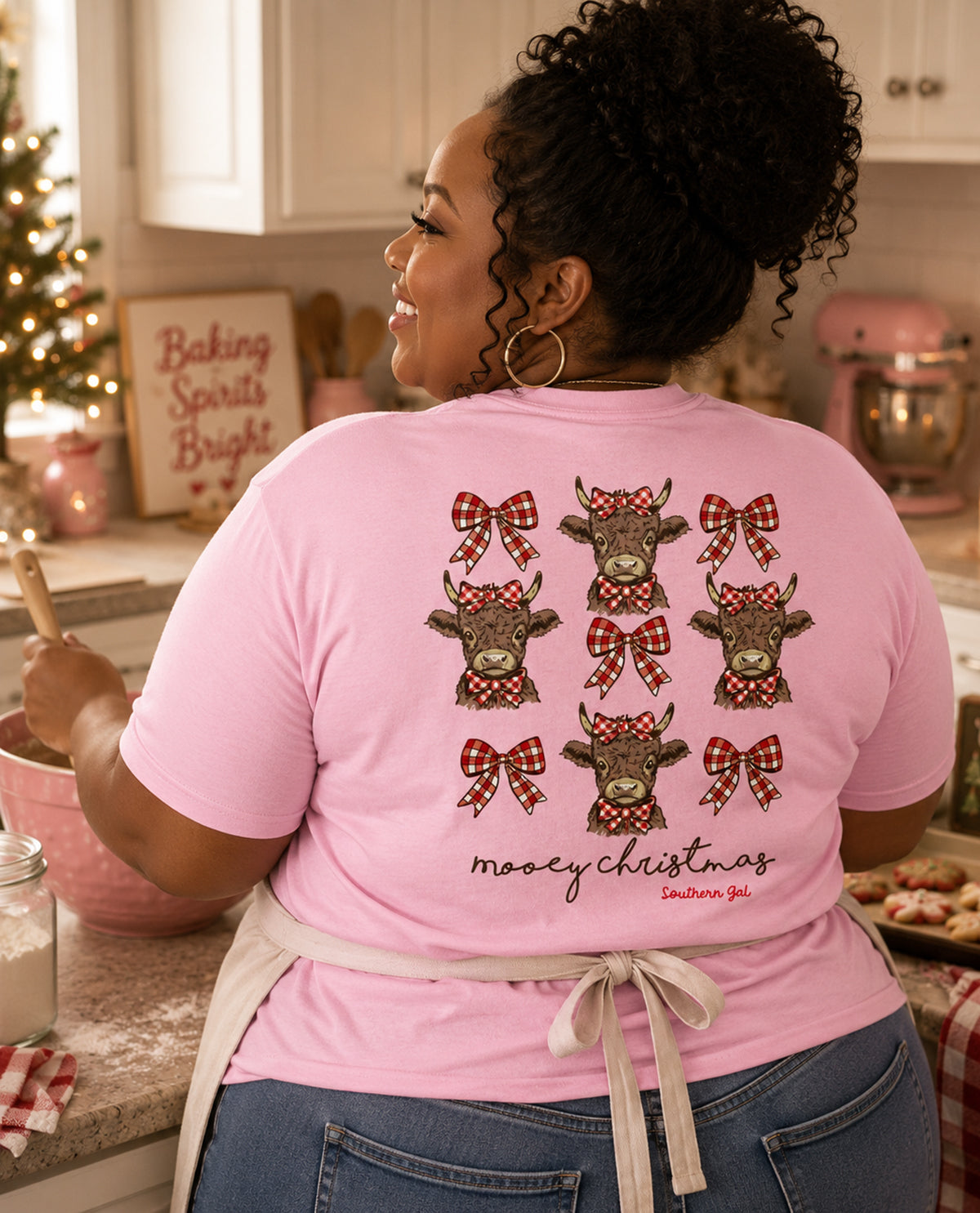 Person wearing a pink t-shirt with Christmas-themed cow designs in a kitchen.