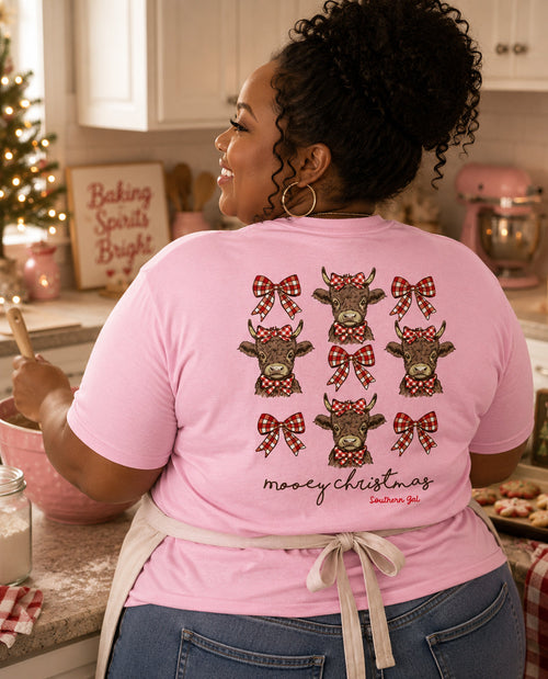 Person wearing a pink t-shirt with Christmas-themed cow designs in a kitchen.