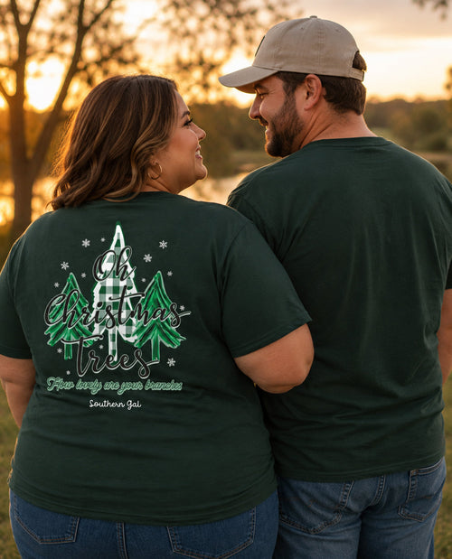 Two people wearing green t-shirts with a Christmas tree design, standing in a field at sunset.