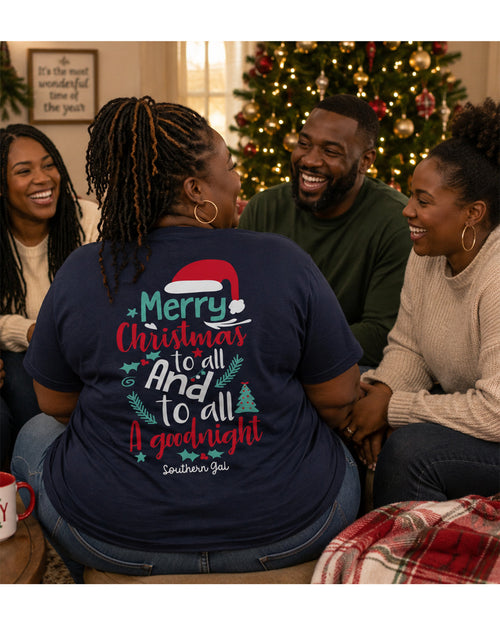 Person wearing a Christmas-themed t-shirt with friends around a Christmas tree.