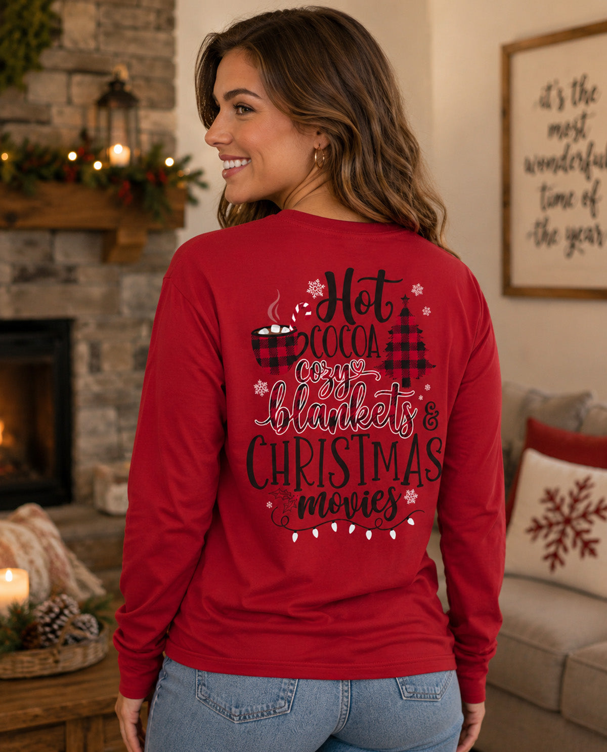 A woman wearing a red long-sleeve graphic shirt, shown from the back in a cozy living room setting with a fireplace and holiday decor.
