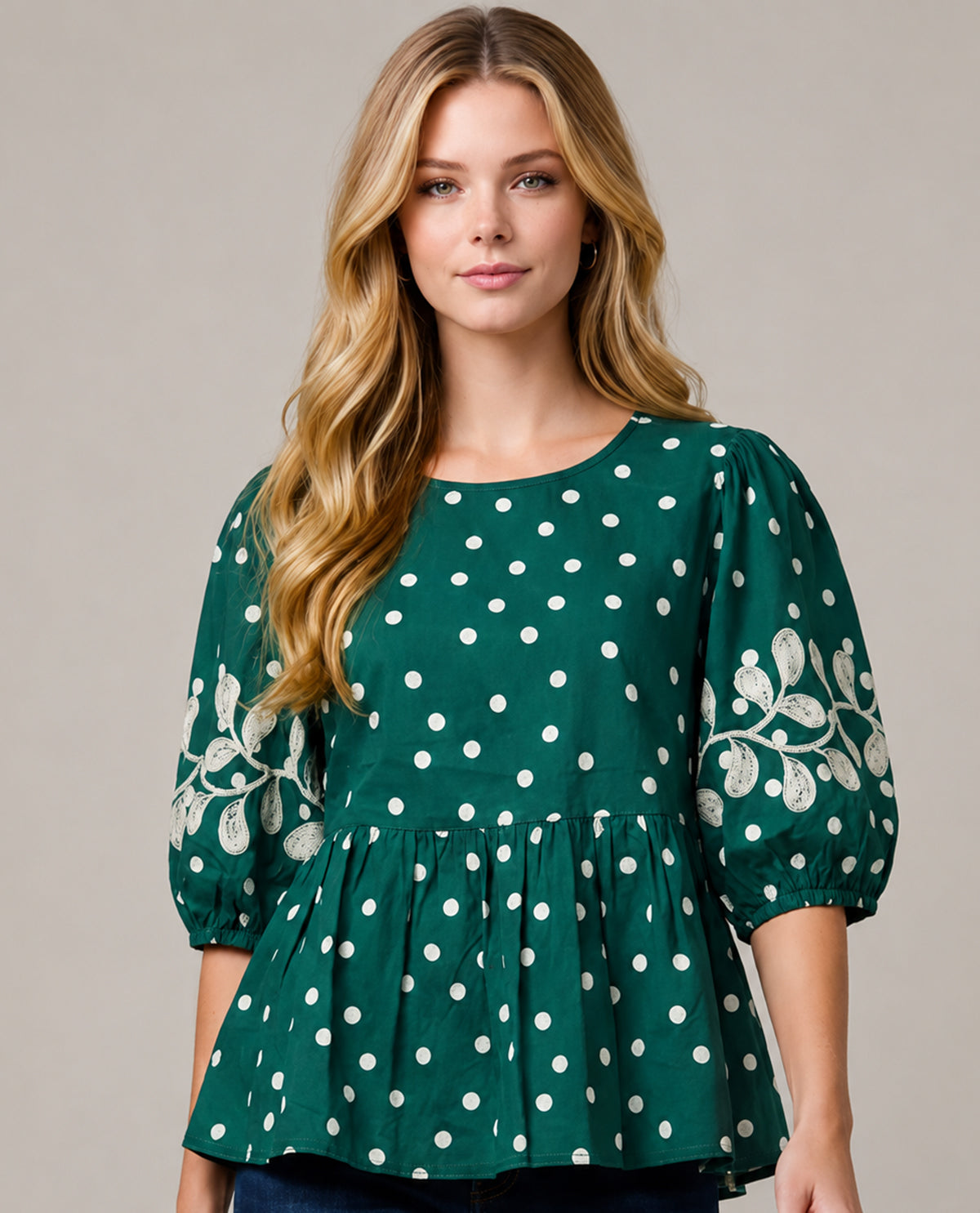 Woman wearing a green blouse with white polka dots and floral patterns on a plain background