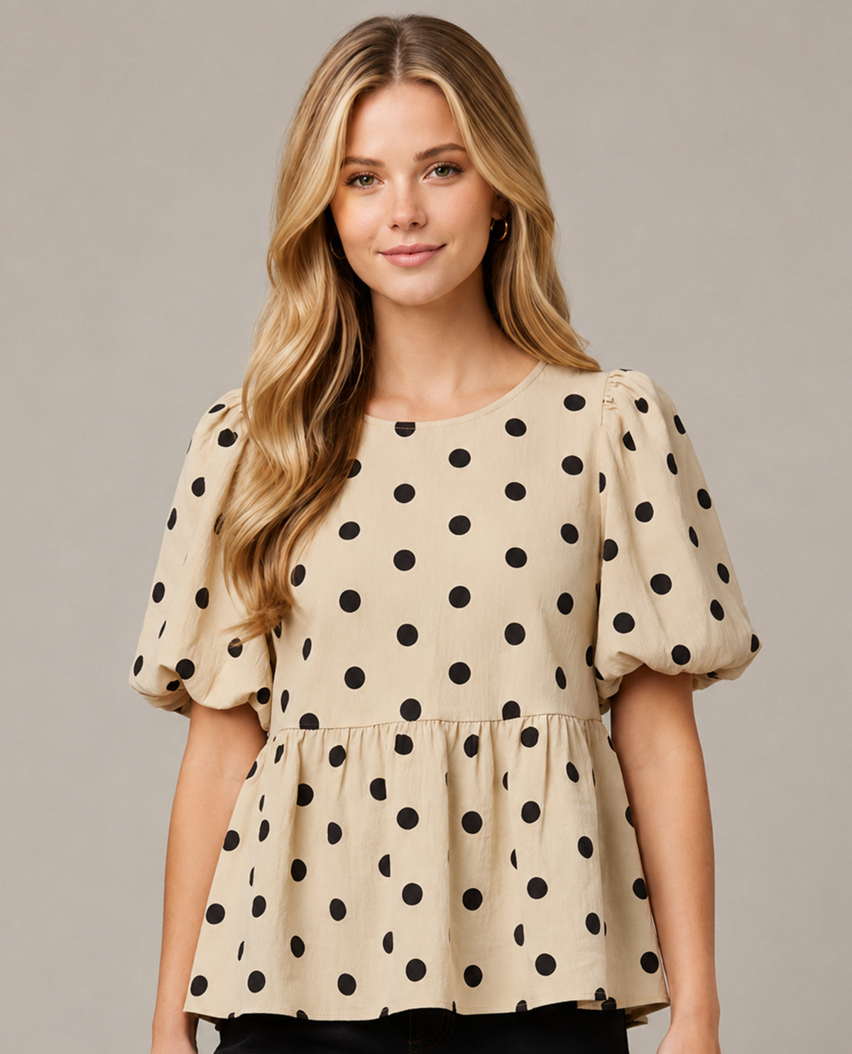 Woman wearing a beige blouse with black polka dots on a plain background