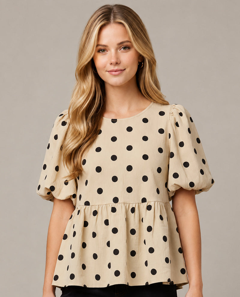 Woman wearing a beige blouse with black polka dots on a plain background