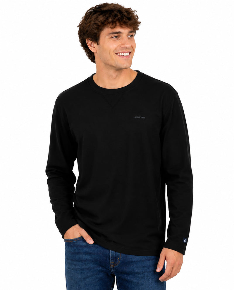A smiling man with brown hair wearing a black long-sleeve crewneck shirt and blue jeans, standing against a plain white background.
