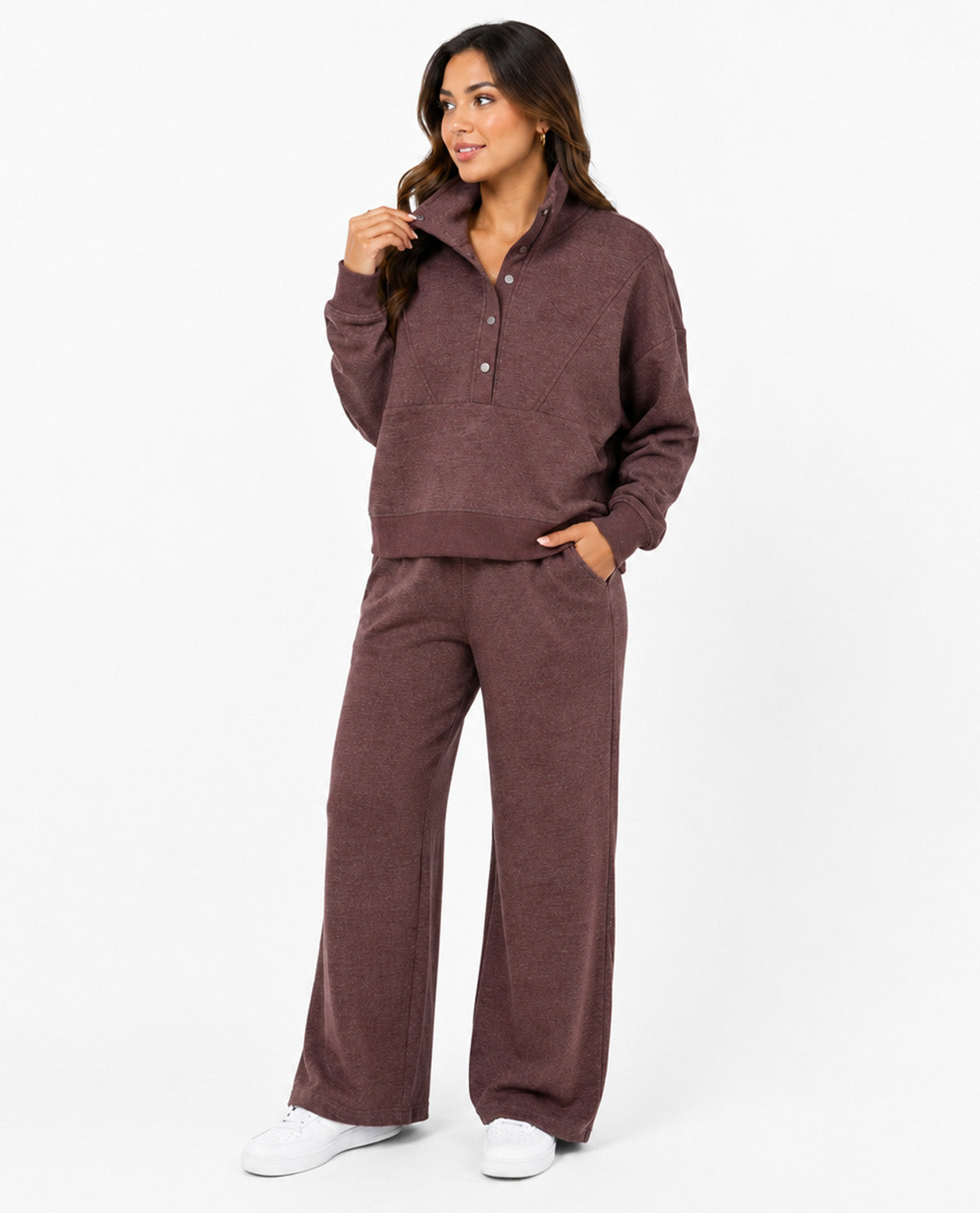 A woman modeling a matching two-piece lounge set in a heathered dark brown color, featuring a long-sleeve half-button pullover and wide-leg pants, paired with white sneakers against a plain white studio background.