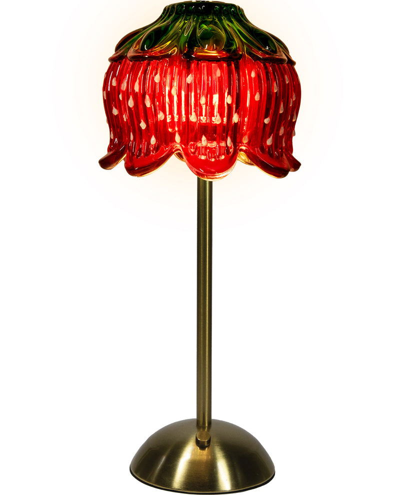 A strawberry-themed table lamp with a red and green glass shade, a brass-colored stem, and a round brass base, shown against a plain white background.