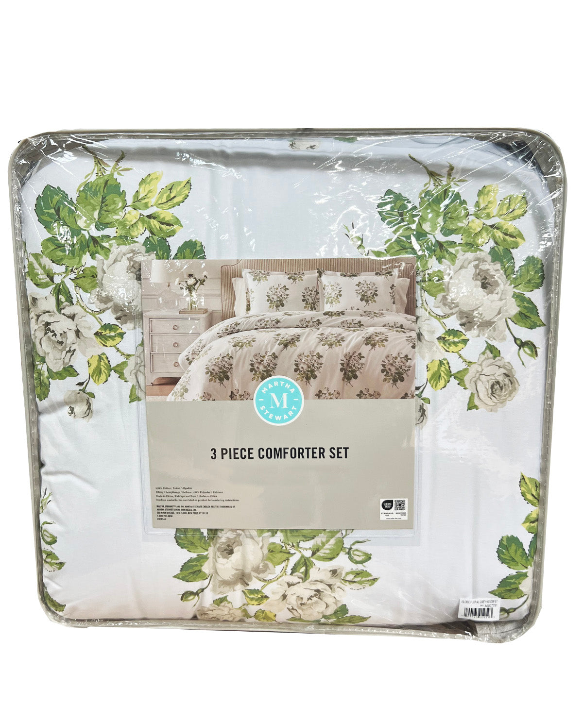 A packaged 3-piece comforter set with a floral print, featuring white and beige roses with green leaves. The set is wrapped in clear plastic with a paper label in the center that reads '3 PIECE COMFORTER SET' and shows a bedroom mockup.