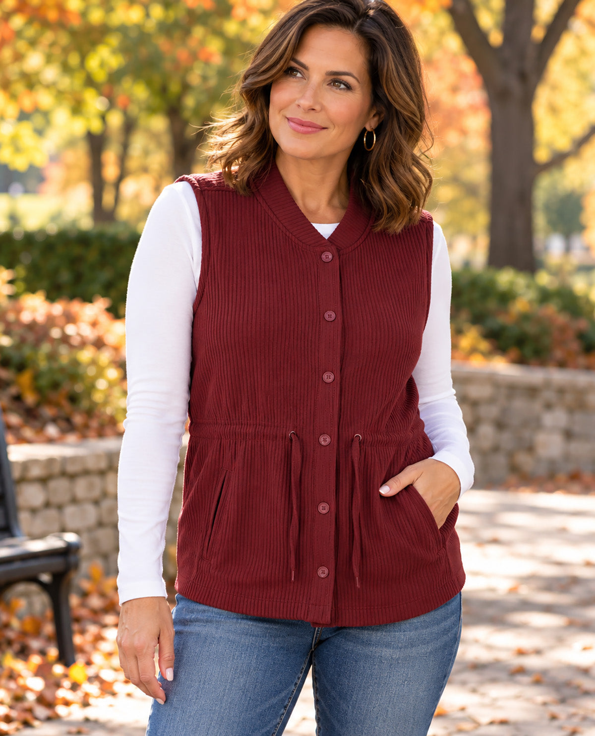 Missy model wearing a burgundy vest with a white long sleeve underneath paired with jeans with an outdoor background
