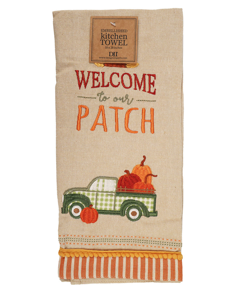 A beige linen kitchen towel featuring embroidered autumn-themed graphics. The design includes the text 'WELCOME to our PATCH' in red and orange, a green and white checkered pickup truck carrying pumpkins, and a striped orange and white fringed hem.
