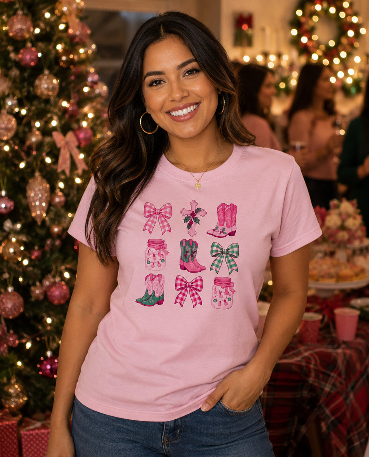 A woman wearing a light pink graphic t-shirt with a grid of cowboy boots and bows in pink, green, and red patterns, posed in front of a decorated Christmas tree.