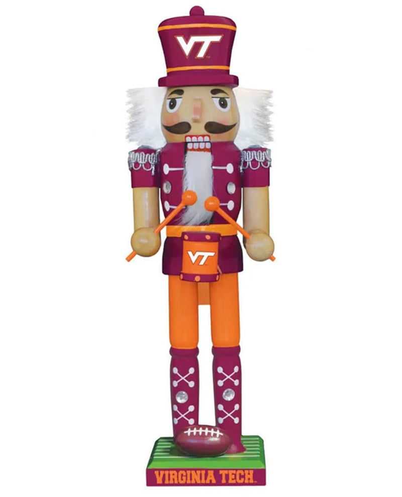 A Virginia Tech football-themed nutcracker figurine standing on a green base labeled 'VIRGINIA TECH'. The nutcracker wears a maroon and gold uniform with white hair, orange pants, and holds orange drumsticks, with a maroon football on its foot.
