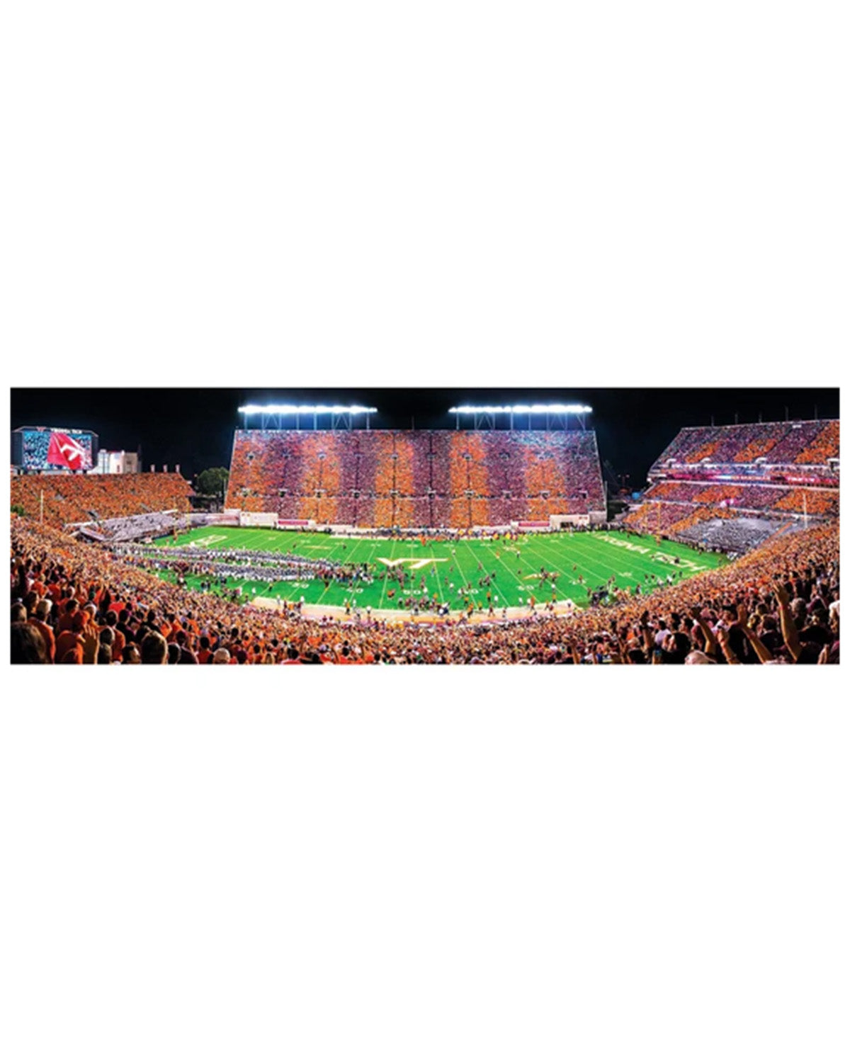 A panoramic stadium scene at night showing a football field surrounded by crowded orange and brown stands under bright stadium lights.