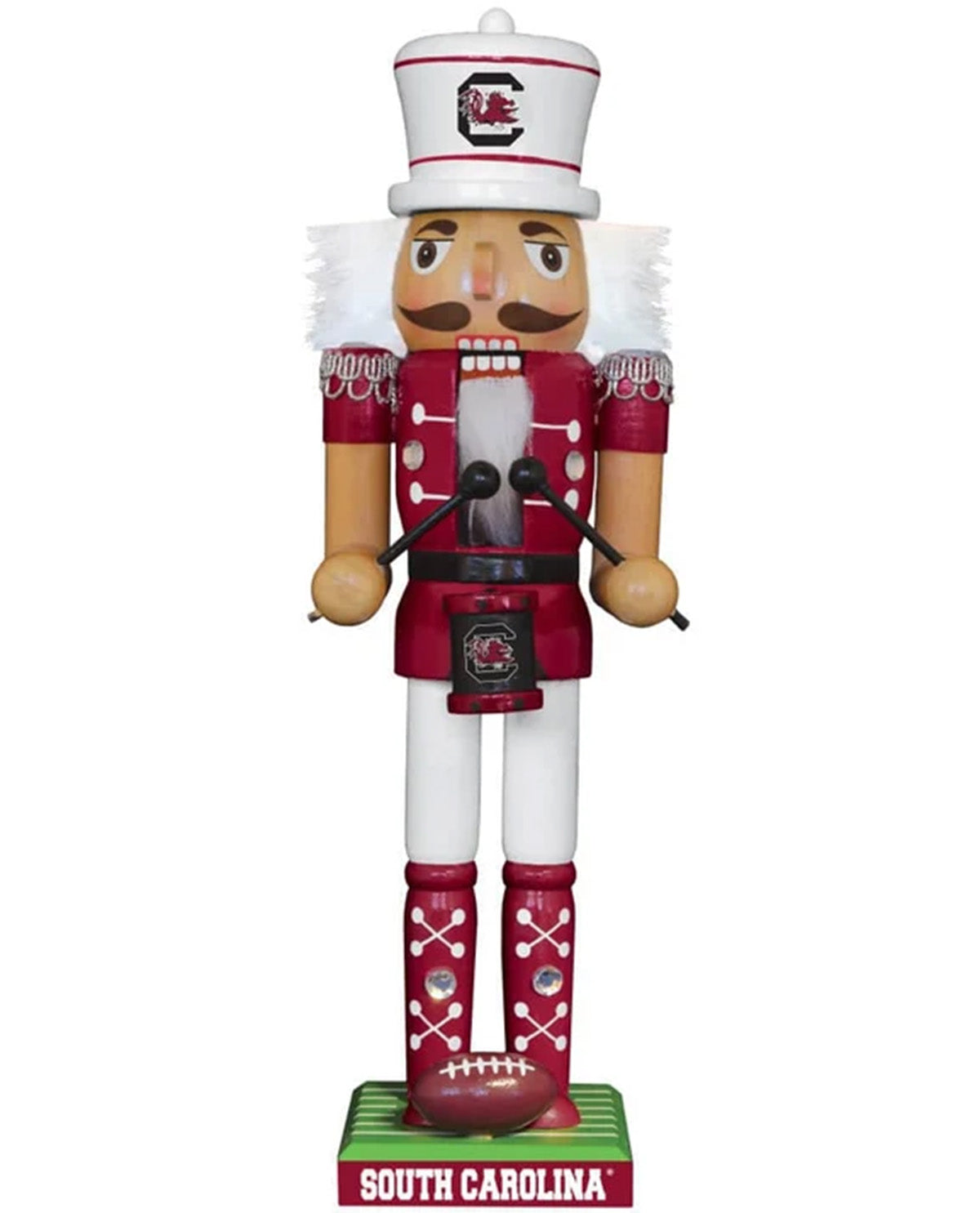 A South Carolina Gamecocks nutcracker figurine standing on a green base labeled 'SOUTH CAROLINA'. The nutcracker is dressed in a red and white uniform with white fur trim, a white hat with a red SC logo, and red boots with white crossed accents.