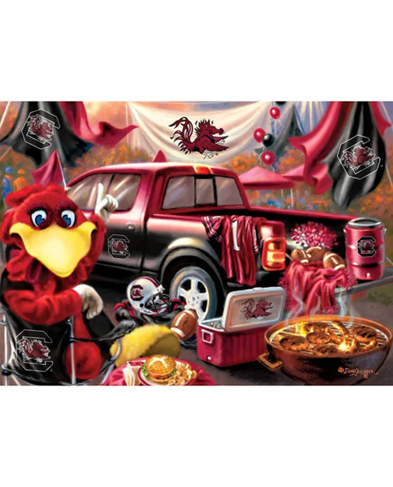 A square jigsaw puzzle featuring a festive South Carolina Gamecocks themed scene. The illustration shows a red truck with a bed rack loaded with food, a red cooler, a bowl of fried chicken, and a red mascot character sitting in a chair.