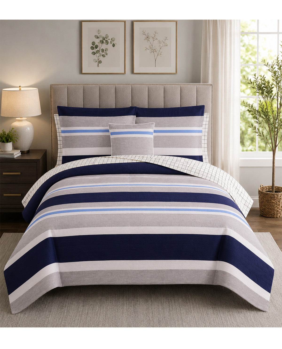 A striped bedding set with navy blue, light blue, gray, and white horizontal stripes, styled on a bed with a tufted headboard in a bright bedroom setting.