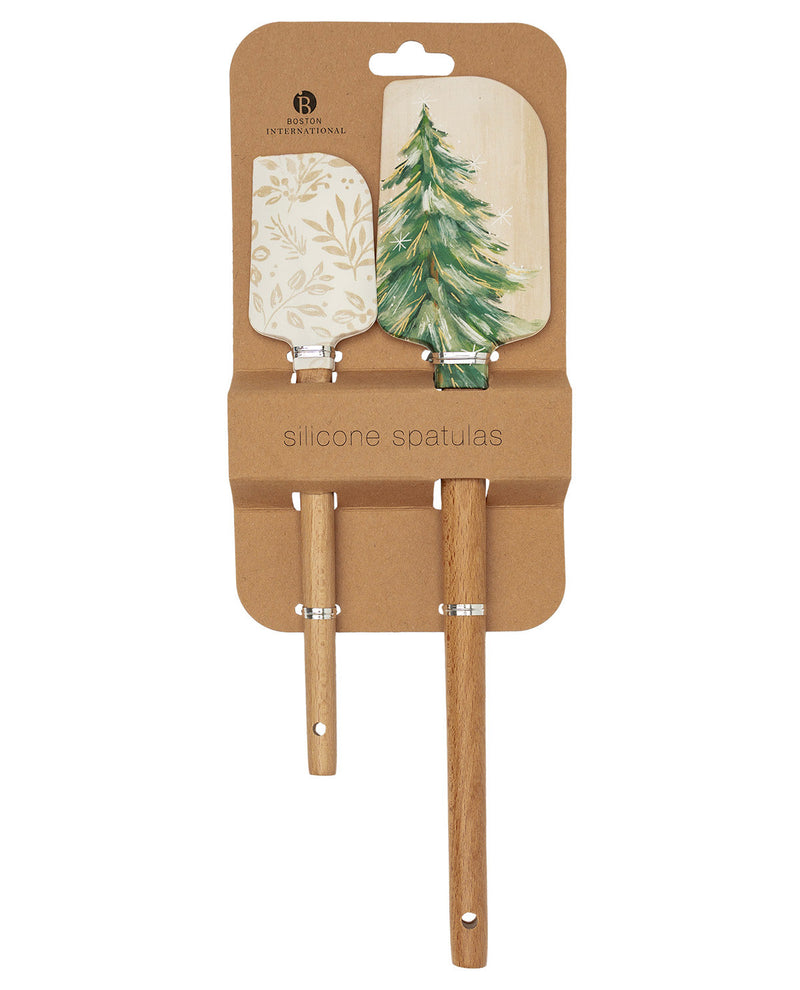 A set of two silicone spatulas with wooden handles, presented on a brown cardboard backing. One spatula has a light beige floral pattern, and the other has a green watercolor pine tree design.