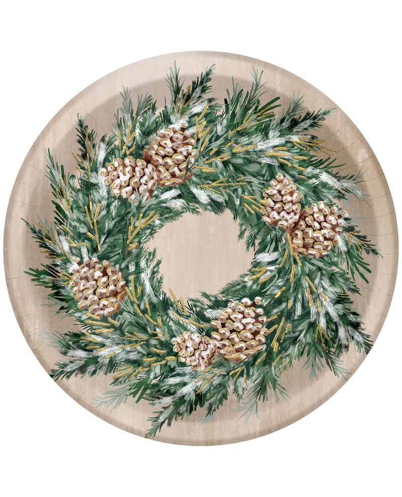 A round paper plate featuring a printed Christmas wreath design with green pine branches, white snow-like dusting, and several beige pinecones on a light beige background.