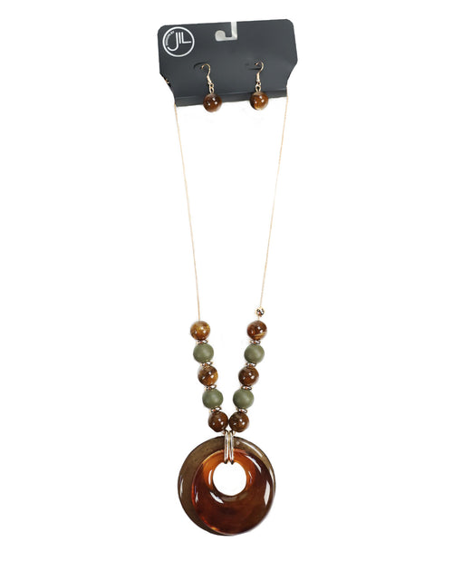 A beaded necklace and matching drop earrings displayed on a black retail card. The necklace has a large translucent amber-brown donut pendant with smaller brown and olive green beads, and the matching earrings have small brown beads and gold hooks.