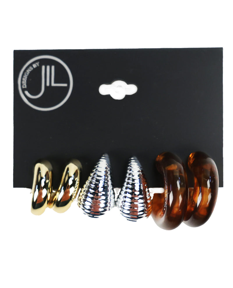 Three pairs of spiral hoop earrings displayed on a black backing card. The left pair is metallic gold, the middle pair is metallic silver with a textured pattern, and the right pair is translucent amber brown.