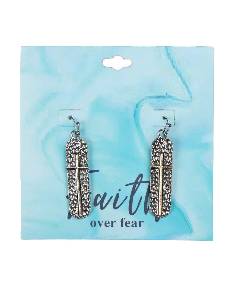 A pair of silver-toned cross dangle earrings with textured, rhinestone-like detailing, displayed on a light blue marbled backing card with the text 'faith over fear'.