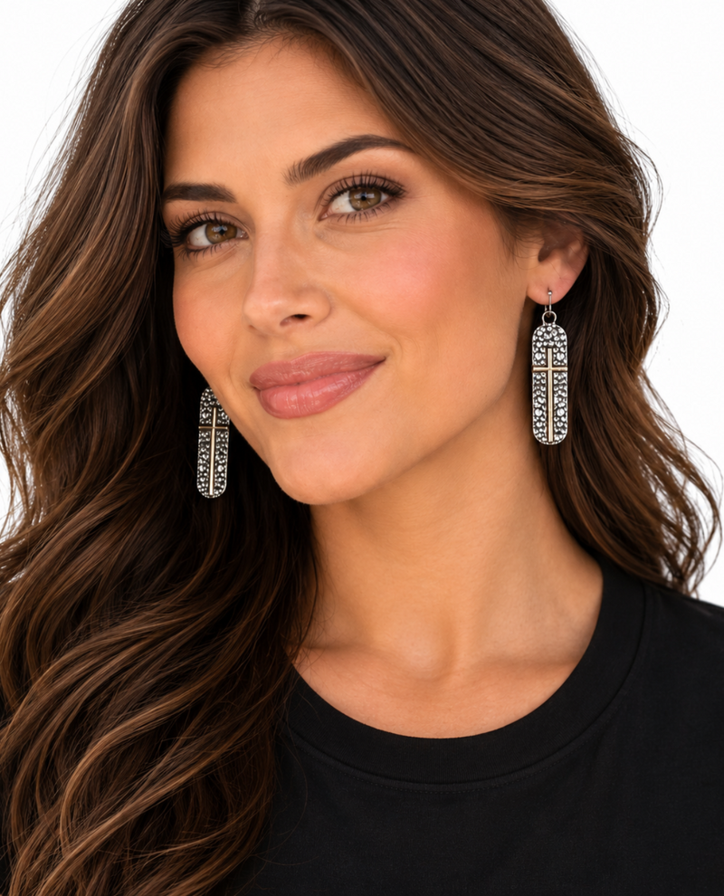 A close-up of a woman with long brown hair wearing a pair of silver-toned drop earrings with intricate filigree detailing, set against a clean white background.