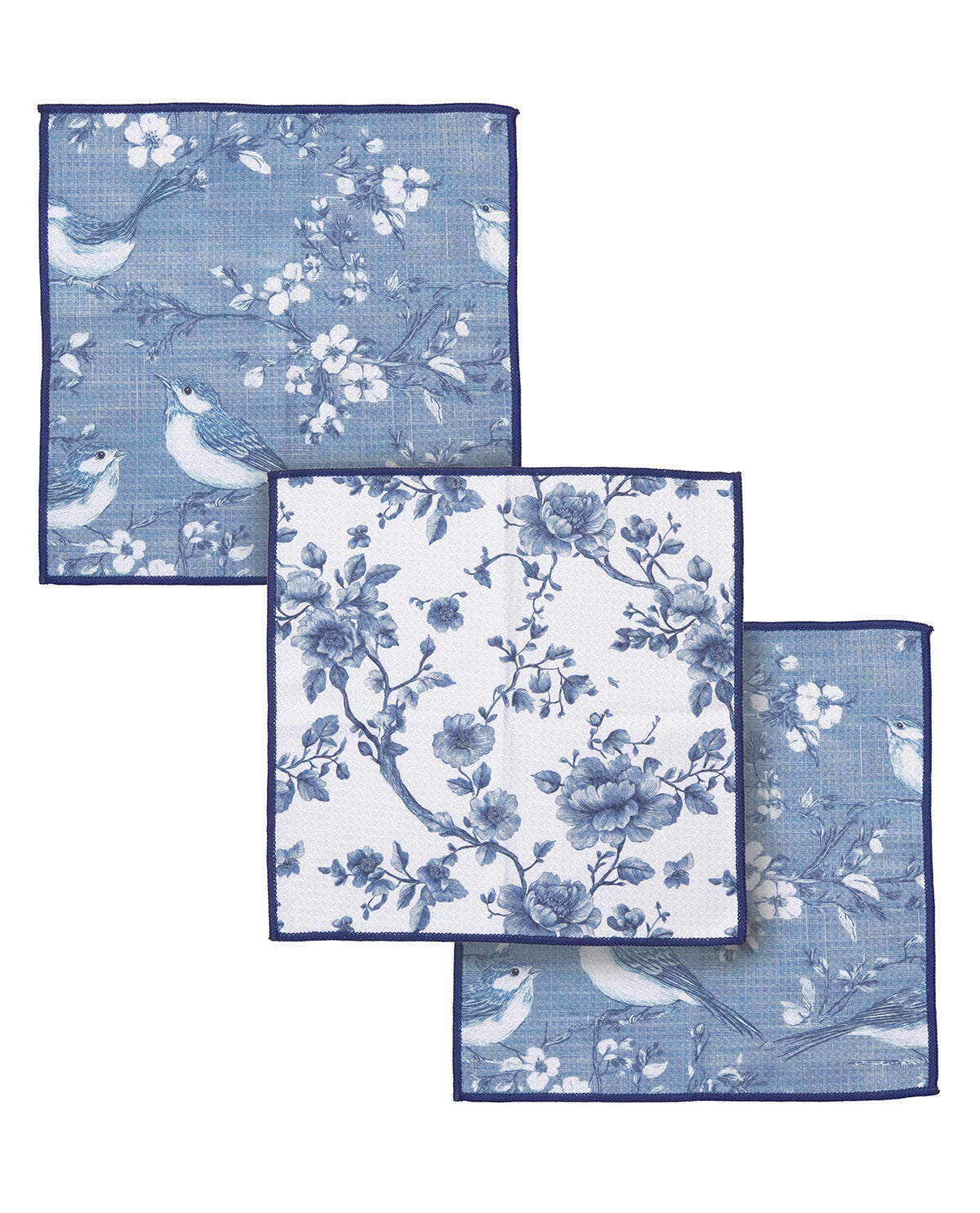 Three square blue patterned cloth napkins with navy borders, arranged overlapping on a white background. The napkins feature floral and bird motifs in varying densities.
