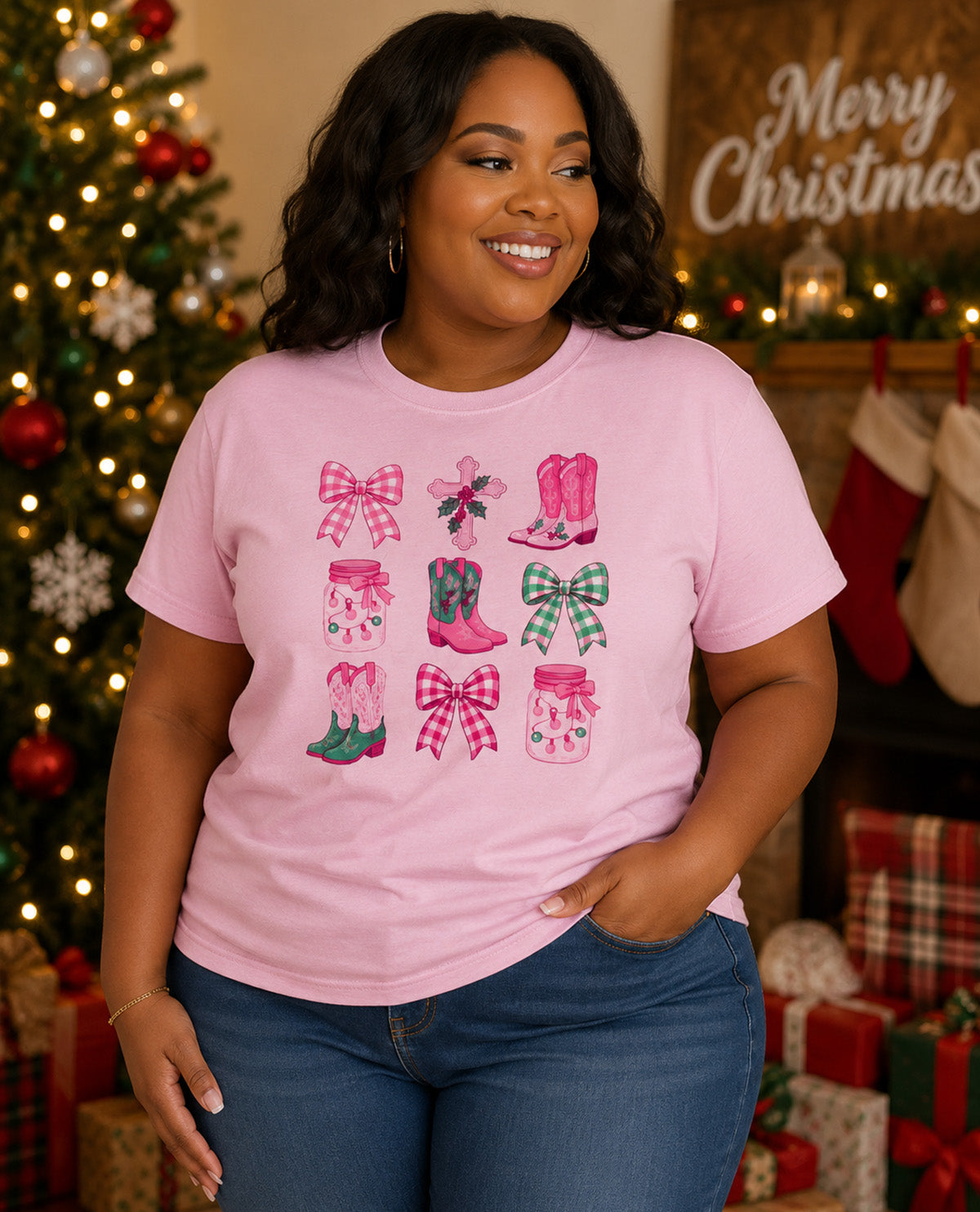 A woman wearing a light pink graphic t-shirt with a Christmas boot and bow pattern, posed in front of a decorated Christmas tree and fireplace.