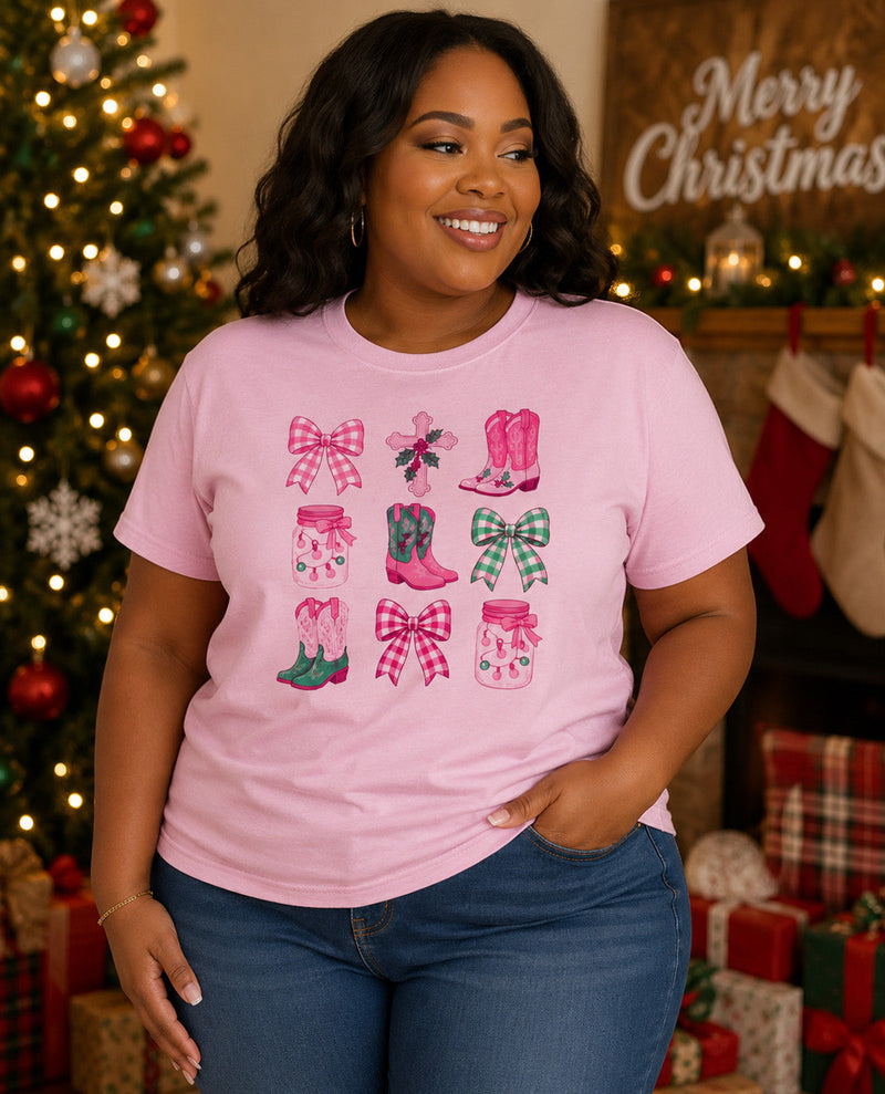 A woman wearing a light pink graphic t-shirt with a Christmas boot and bow pattern, posed in front of a decorated Christmas tree and fireplace.