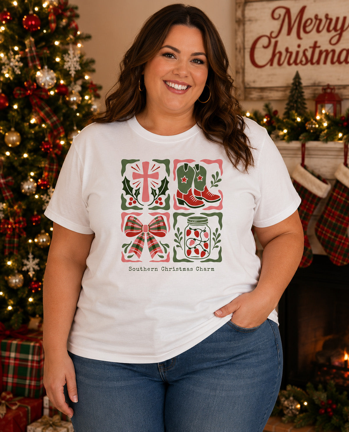 A woman wearing a white graphic t-shirt with a Christmas-themed print, standing in a cozy holiday living room setting with a decorated Christmas tree and fireplace in the background.