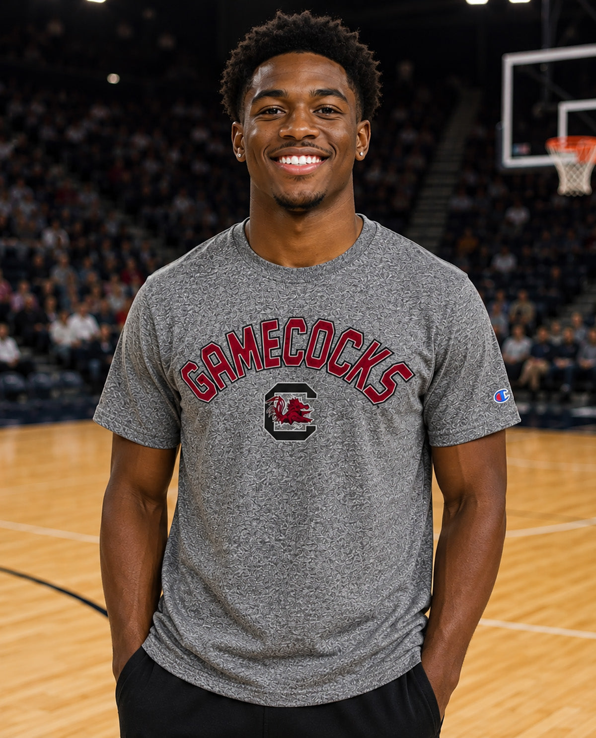 A smiling man standing on a basketball court wearing a heather gray Champion t-shirt with 'GAMECOCKS' and a red logo printed on the front.
