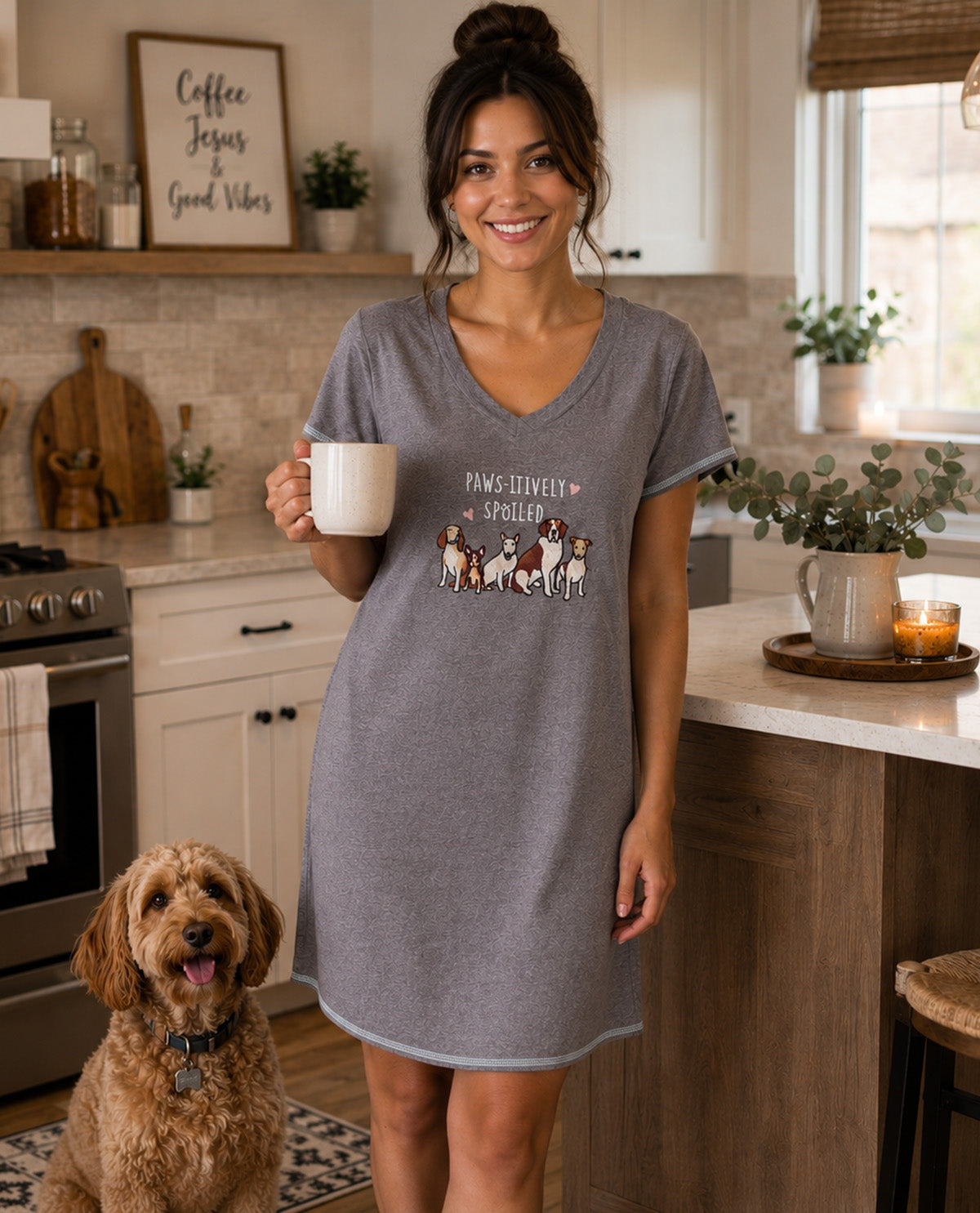 A woman wearing a heather gray V-neck sleep shirt dress stands in a kitchen holding a white mug, with a small graphic of dogs and the text 'Pawfectly Happy Dogs' on the front. A brown poodle dog sits on the floor nearby.